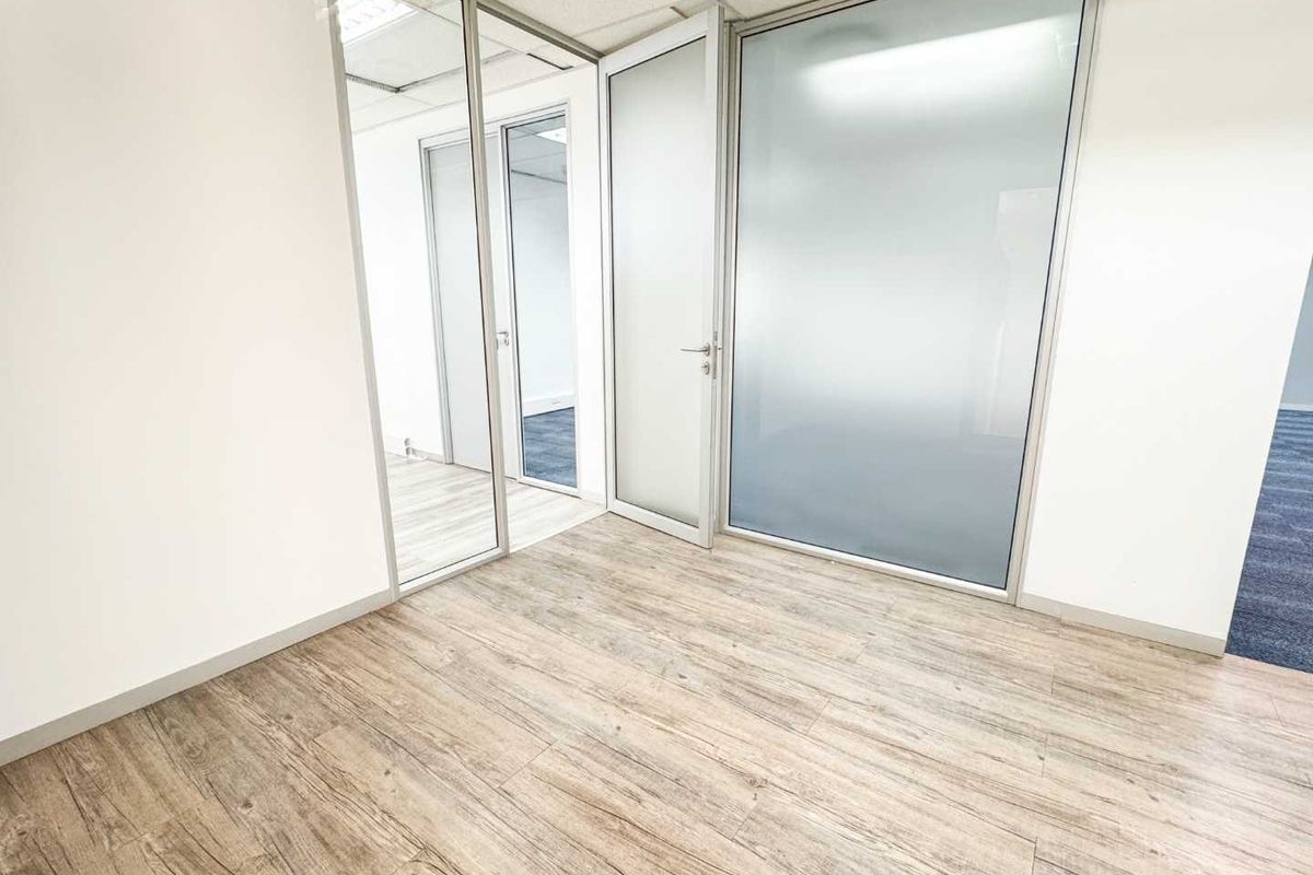 A bright, modern office space featuring wood-look laminate flooring and professional aluminium-framed glass partitions with frosted privacy panels.