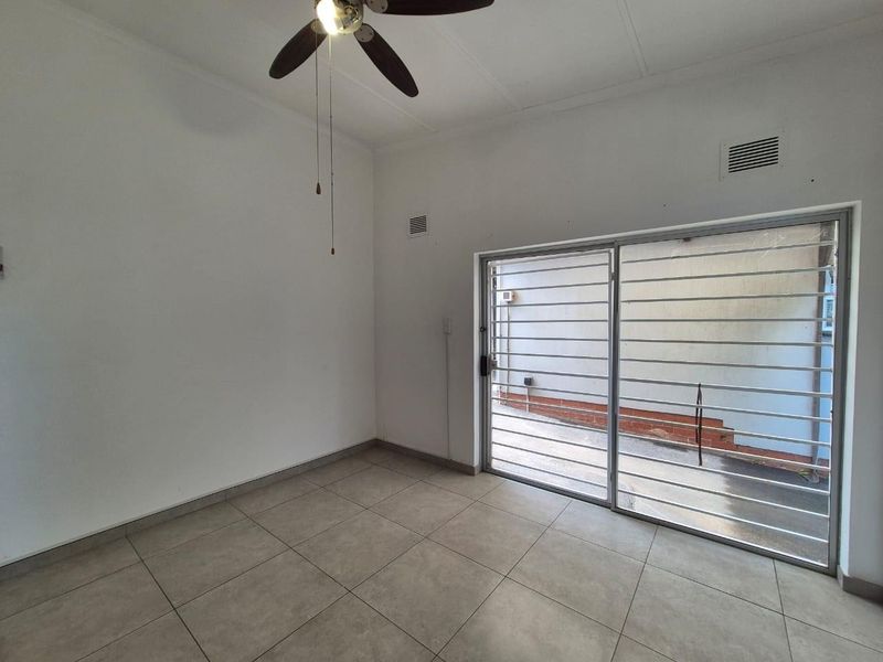 An empty living room featuring tiled flooring, a ceiling fan, and a sliding glass door with security bars leading to an outdoor area.