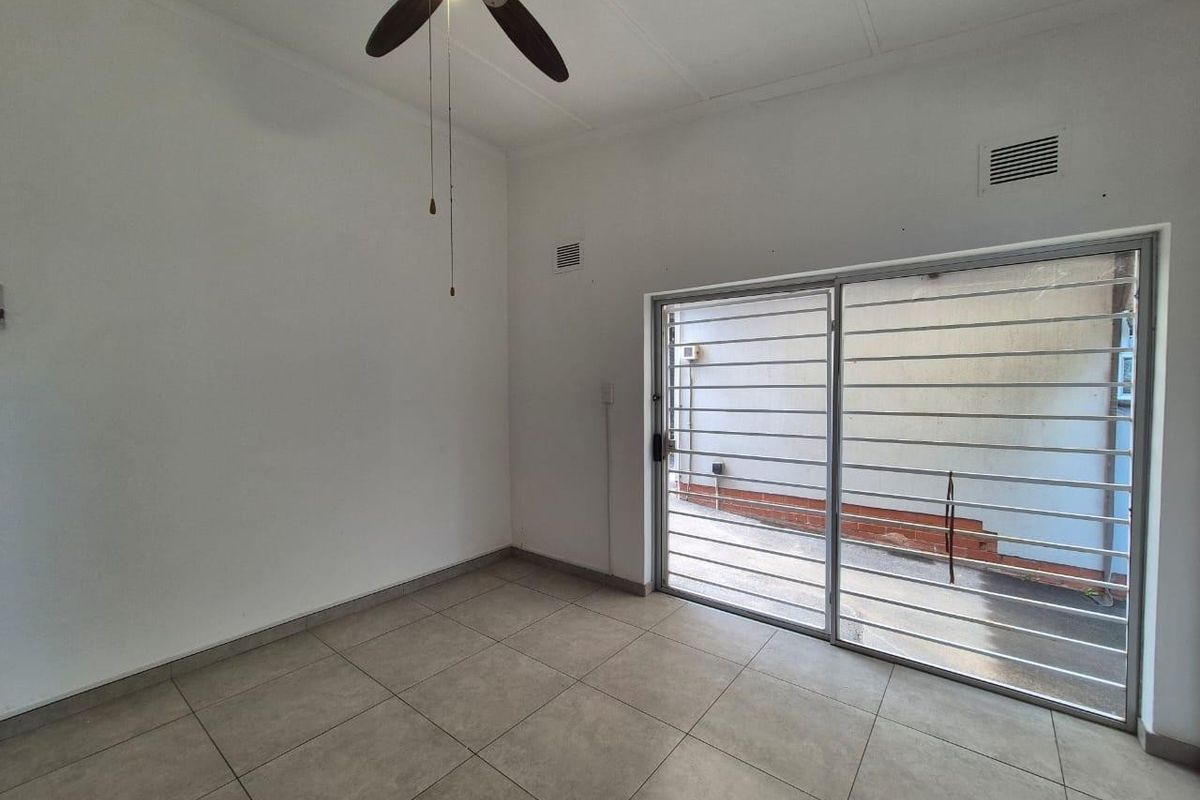 An empty living room featuring tiled flooring, a ceiling fan, and a sliding glass door with security bars leading to an outdoor area.