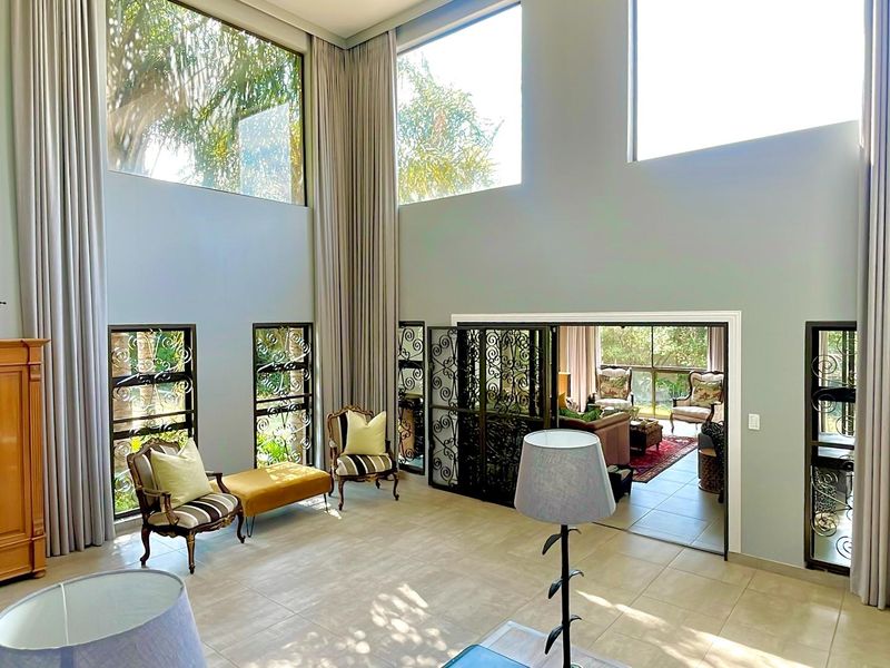Spacious double-volume living area featuring high ceilings, large windows for natural light, and elegant wrought iron security gates leading to an adjacent room.