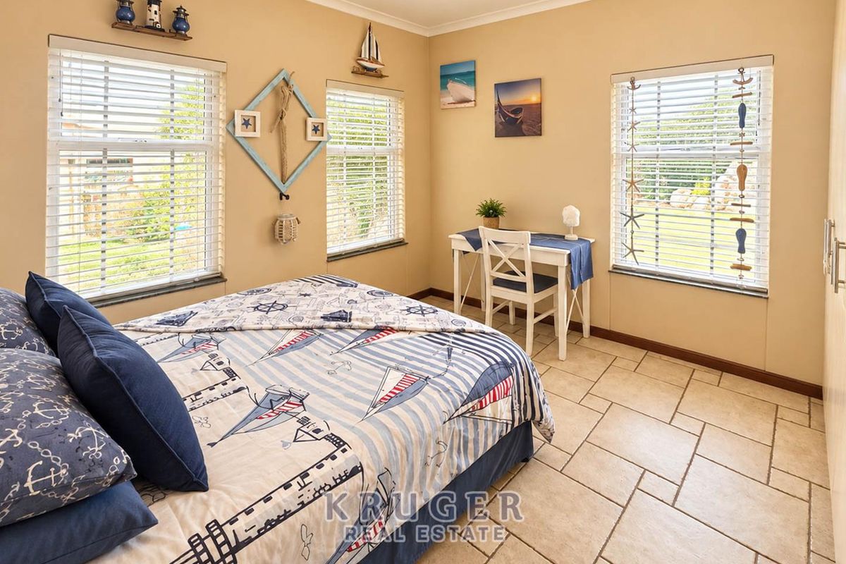 A bright bedroom featuring tiled flooring, built-in wardrobe storage, and multiple windows fitted with venetian blinds, offering a clean and functional living space.