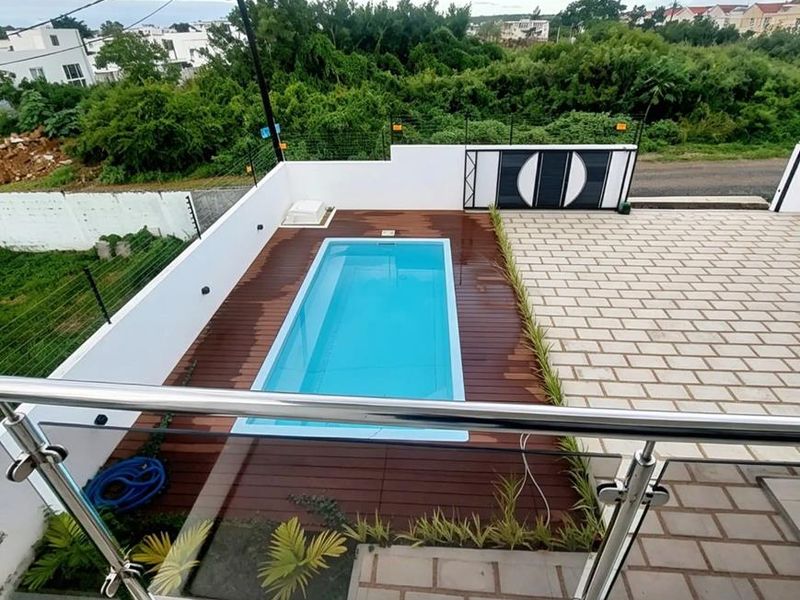 An elevated view of a modern outdoor pool area featuring a rectangular swimming pool, timber decking, and paved patio space.