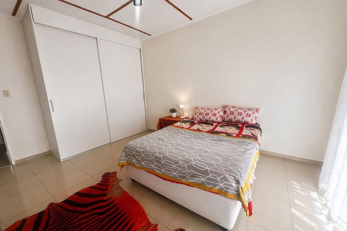 A well-maintained bedroom featuring neutral tiled flooring, a built-in sliding door wardrobe, and a ceiling fan.