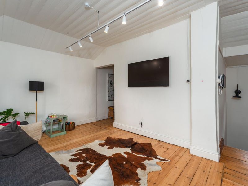 A living room featuring timber flooring, a vaulted timber ceiling, and track lighting, creating a cozy and character-filled space.