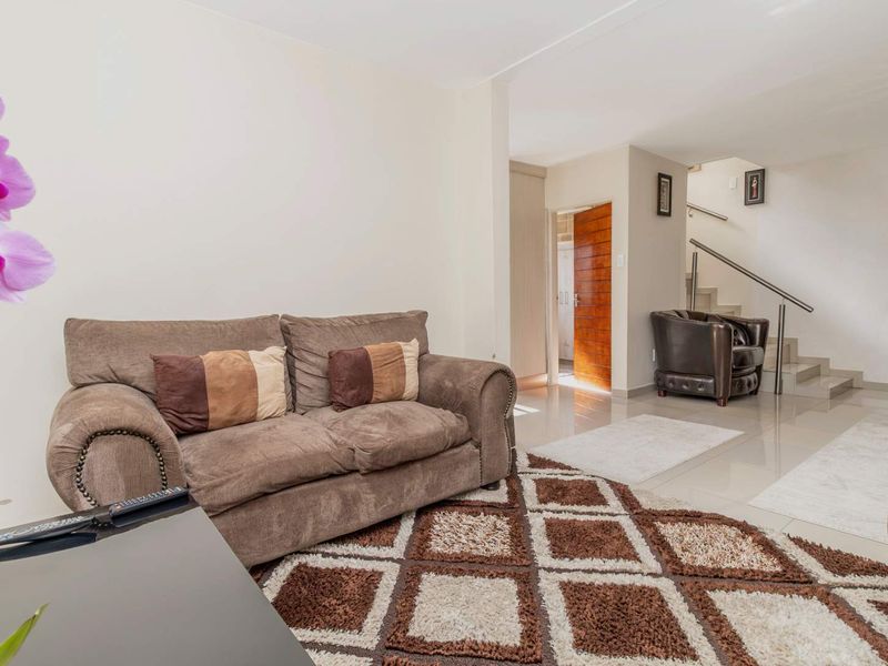 A bright living room featuring polished tiled flooring and an open-plan staircase with a modern metal handrail leading to the upper level.