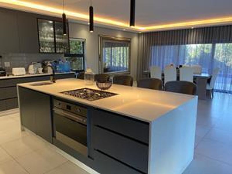 Modern open-plan kitchen featuring a large central island with integrated gas cooktop, oven, and sleek cabinetry, seamlessly flowing into the dining area.