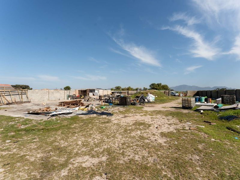 A vacant residential plot featuring a concrete boundary wall and a concrete slab, currently containing various debris and unmaintained ground.