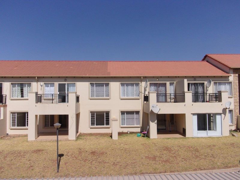 Rear elevation of a multi-story apartment complex featuring terracotta tiled roofing, private balconies with metal railings, and ground-level patio access.