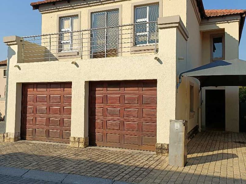Front elevation of a double-story townhouse featuring a double garage, a paved driveway, a carport, and an upper-level balcony with metal railings.