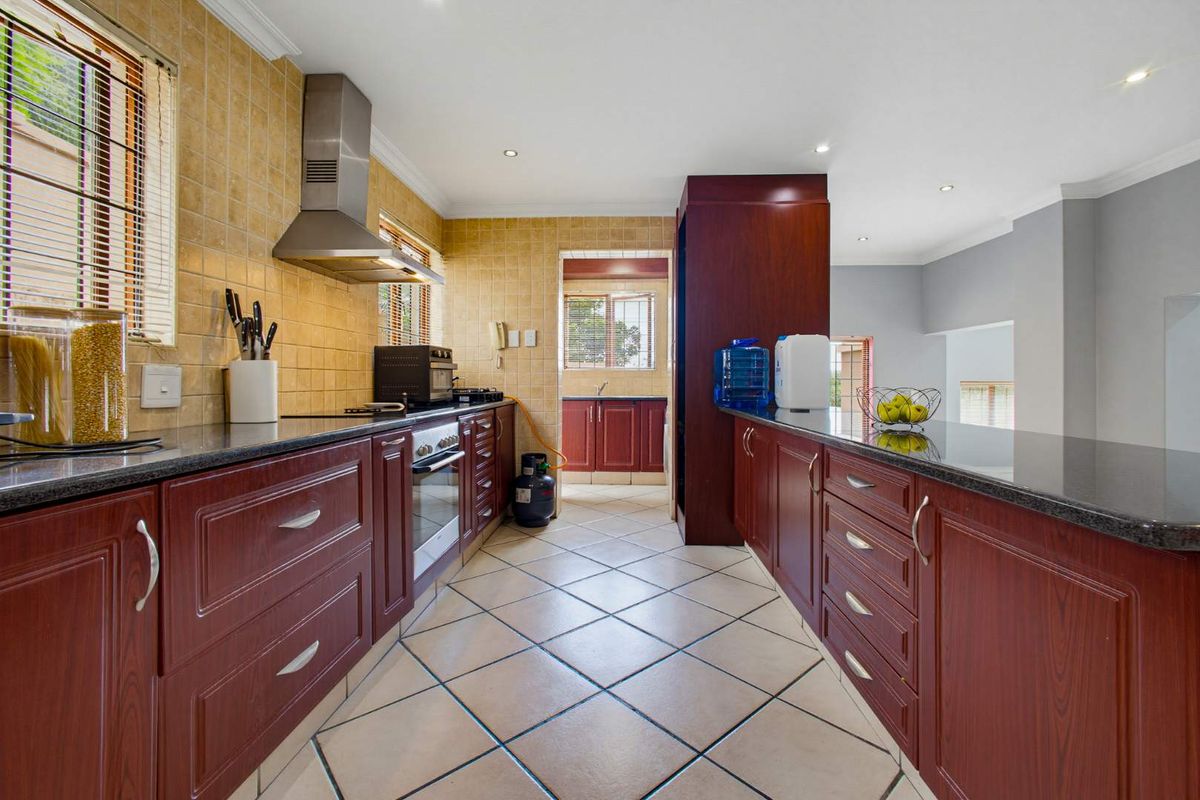 A functional kitchen featuring dark wood cabinetry, granite countertops, tiled backsplash, and built-in appliances, with an adjacent scullery area.