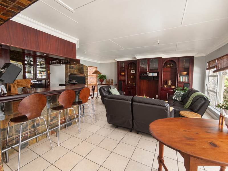 Spacious entertainment area featuring a built-in bar with stone cladding, integrated cabinetry, and a fireplace, finished with neutral floor tiles.