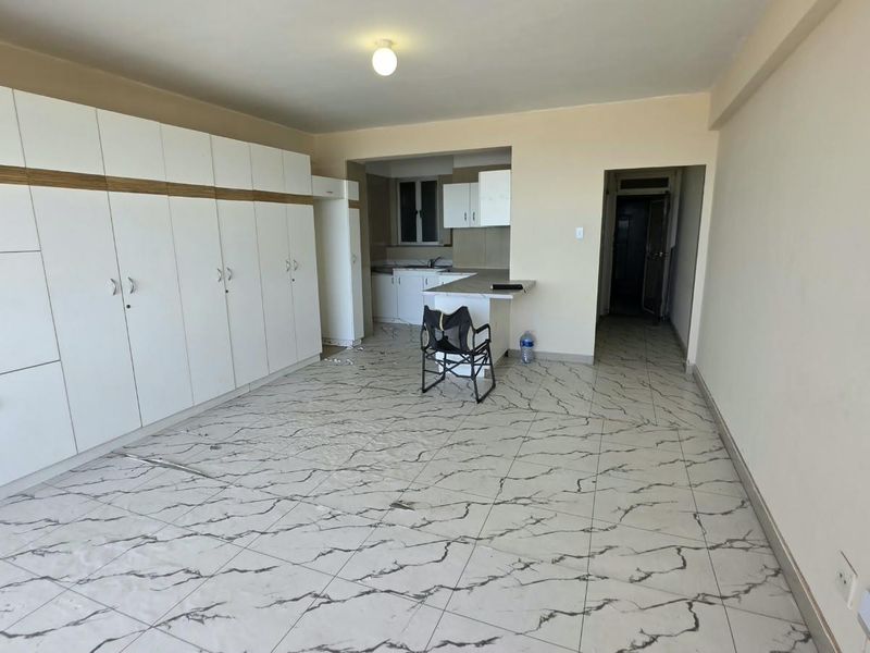Open plan living and kitchen area featuring extensive built-in storage cabinetry, marble-effect tiled flooring, and a breakfast bar counter.