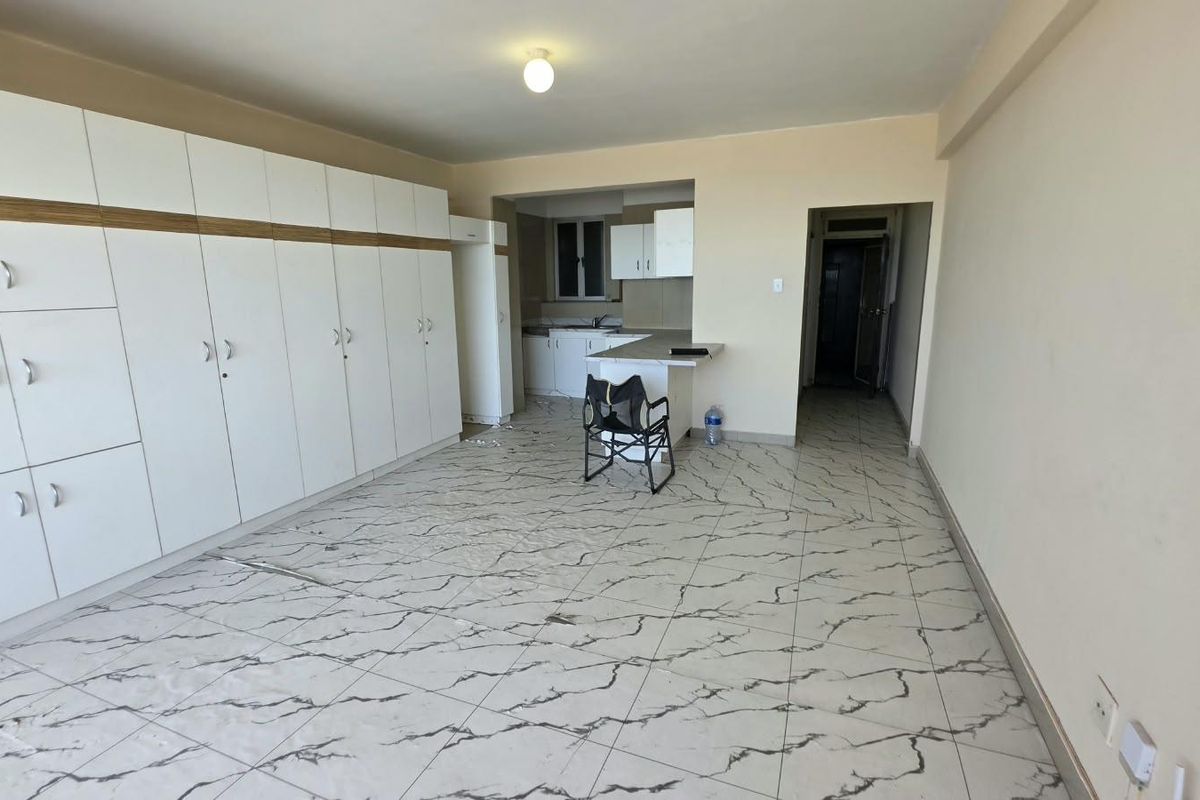 Open plan living and kitchen area featuring extensive built-in storage cabinetry, marble-effect tiled flooring, and a breakfast bar counter.