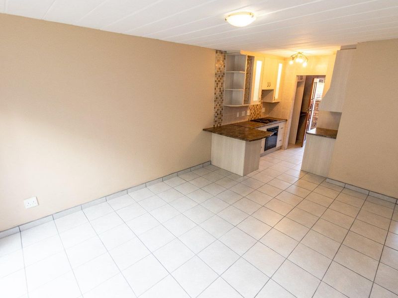 An open-plan living and kitchen area featuring neutral tiled flooring, built-in cabinetry with granite countertops, and a mosaic tile backsplash.