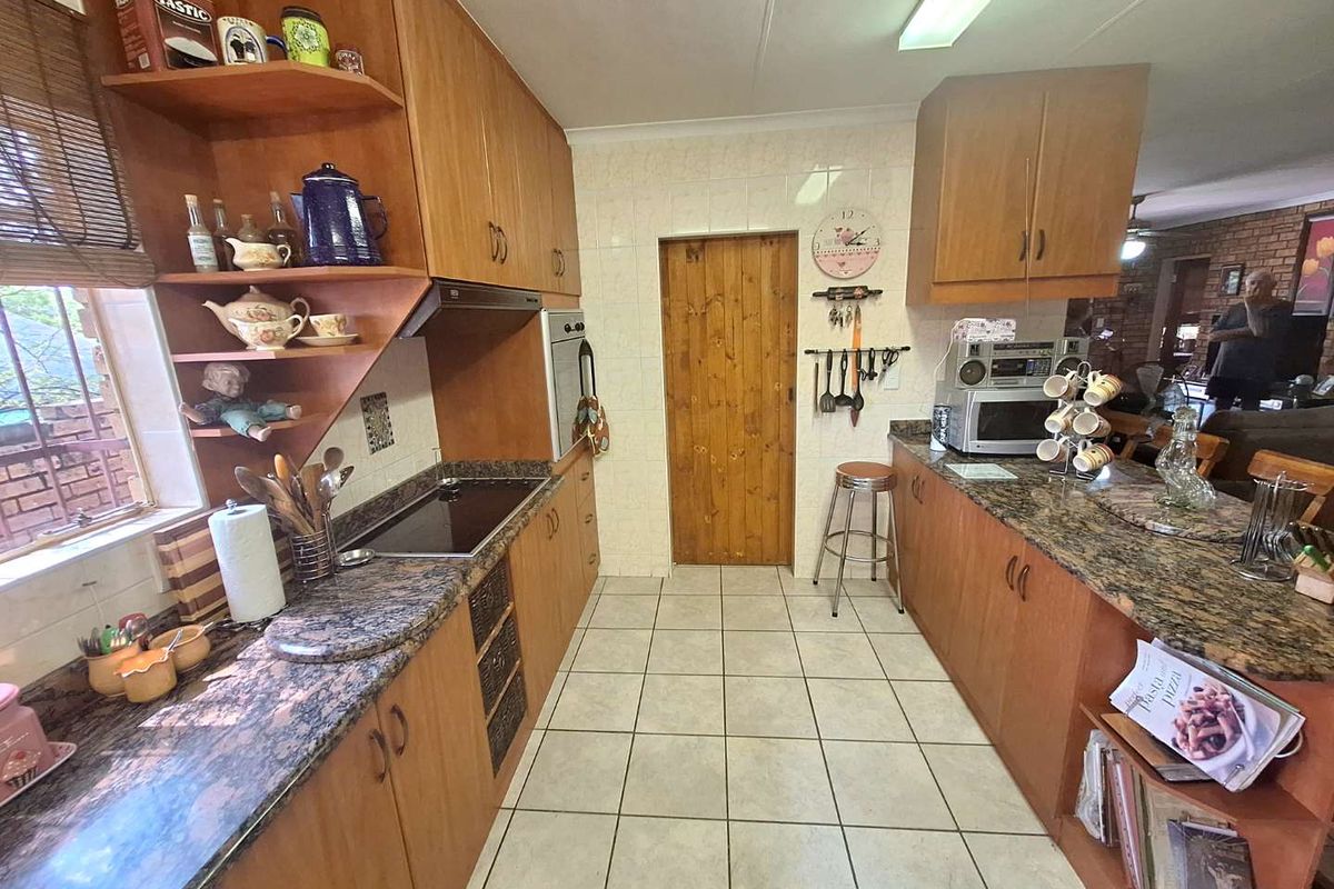 A functional kitchen featuring wood-finish cabinetry, granite-look countertops, a built-in oven, and a ceramic hob, with tiled flooring throughout.