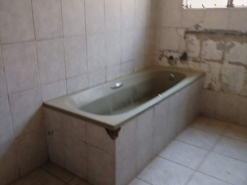 A dated bathroom featuring a built-in bathtub with damaged tiling and exposed wall areas, requiring renovation and cosmetic updates.