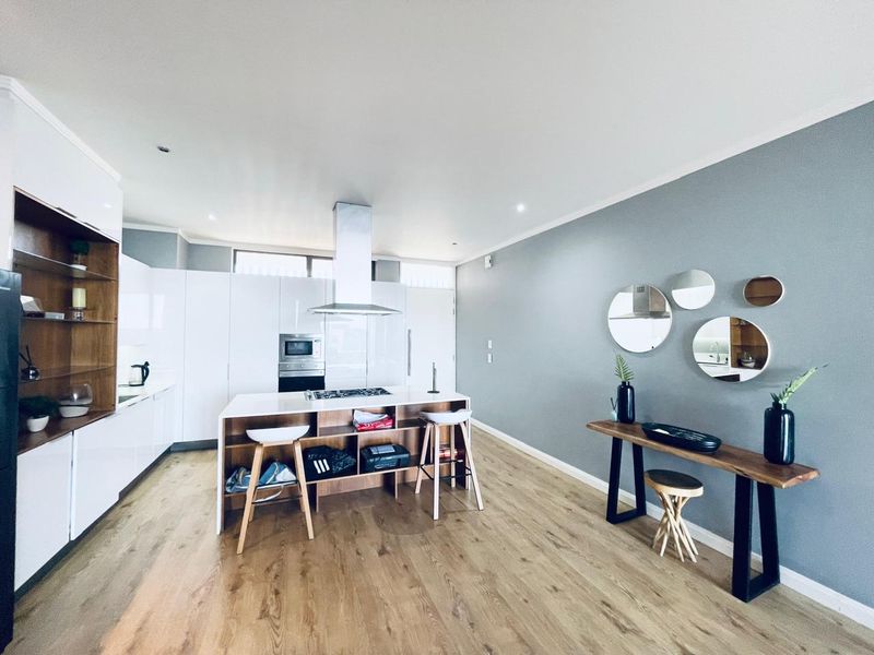 Modern open-plan kitchen featuring a central island with integrated hob, sleek white cabinetry, built-in appliances, and light wood-look flooring.