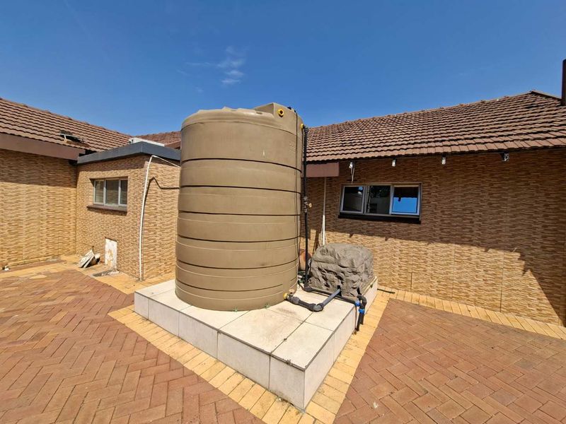 Rear exterior area featuring a large water storage tank installed on a raised tiled platform with brick paving and tiled roof.
