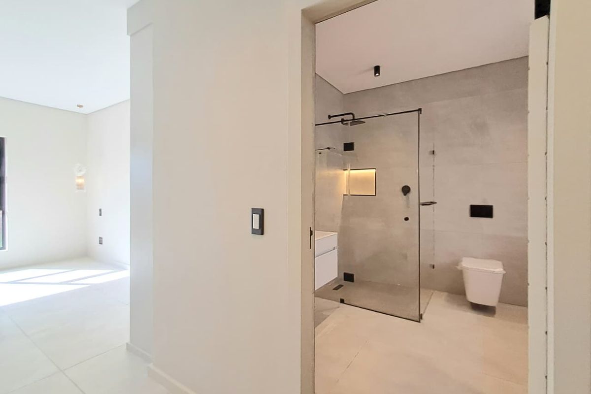 A modern bathroom featuring a frameless glass walk-in shower, wall-mounted toilet, and contemporary grey tiling, viewed from an adjacent hallway.