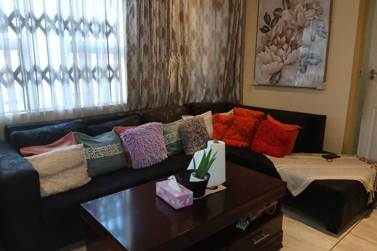 A cozy living room featuring tiled flooring and a window fitted with security bars and curtains.