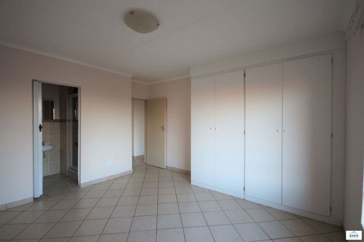 A spacious bedroom featuring neutral tiled flooring, built-in cupboards, and an en-suite bathroom access.