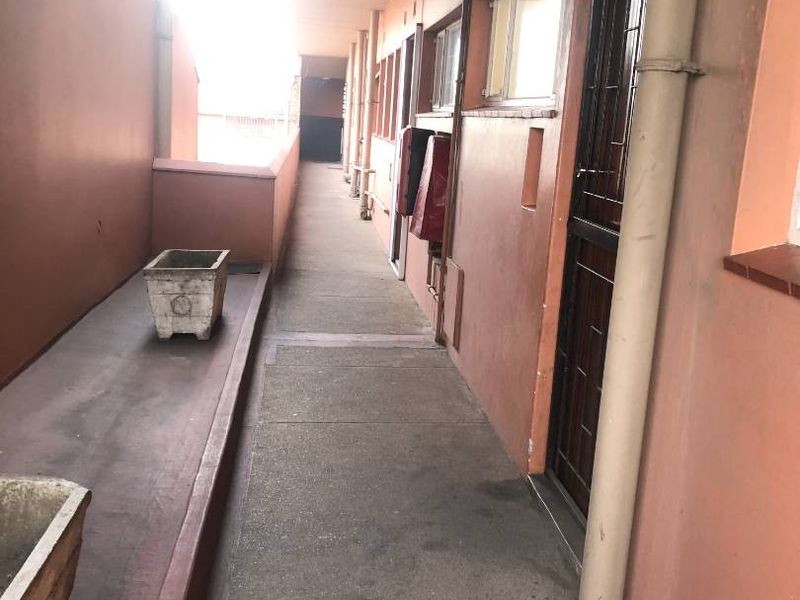 An exterior communal hallway or walkway featuring concrete flooring, security gates, and weathered exterior wall finishes.
