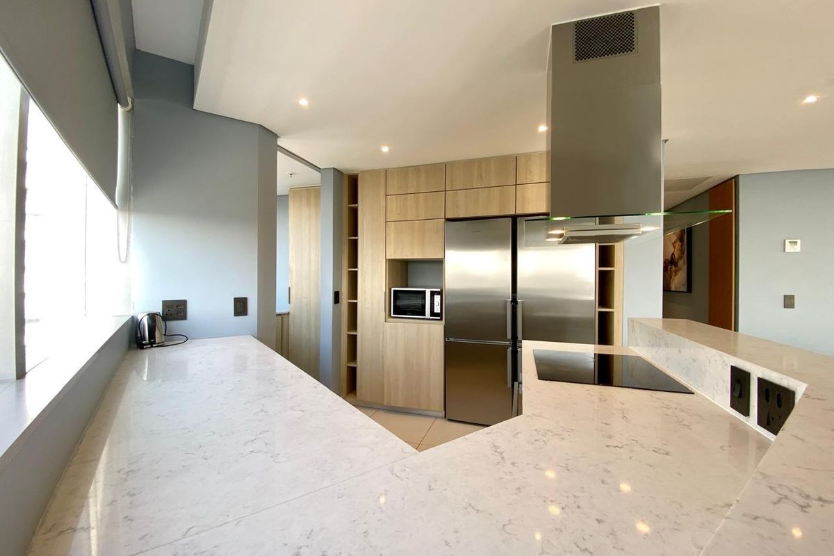 Modern kitchen featuring light wood cabinetry, stone countertops, integrated stainless steel appliances, and a sleek extractor fan.