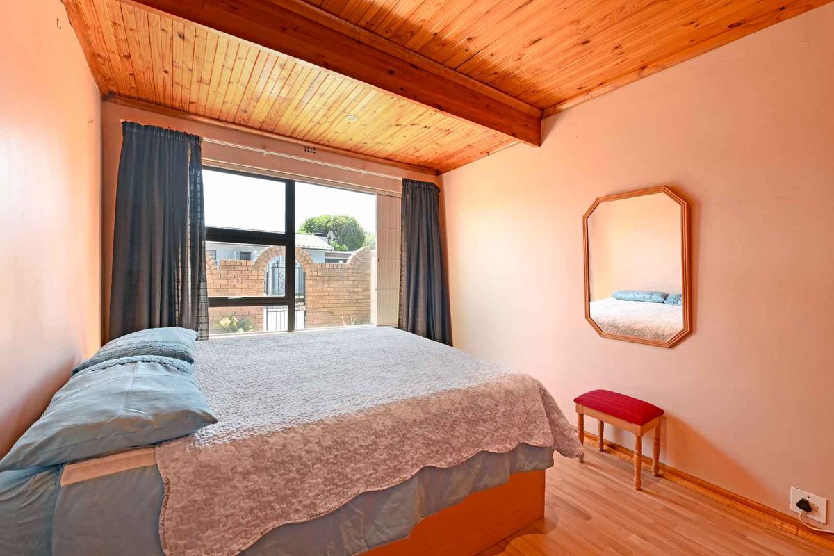 A bedroom featuring a warm timber tongue and groove ceiling, laminate flooring, and a large window providing natural light.