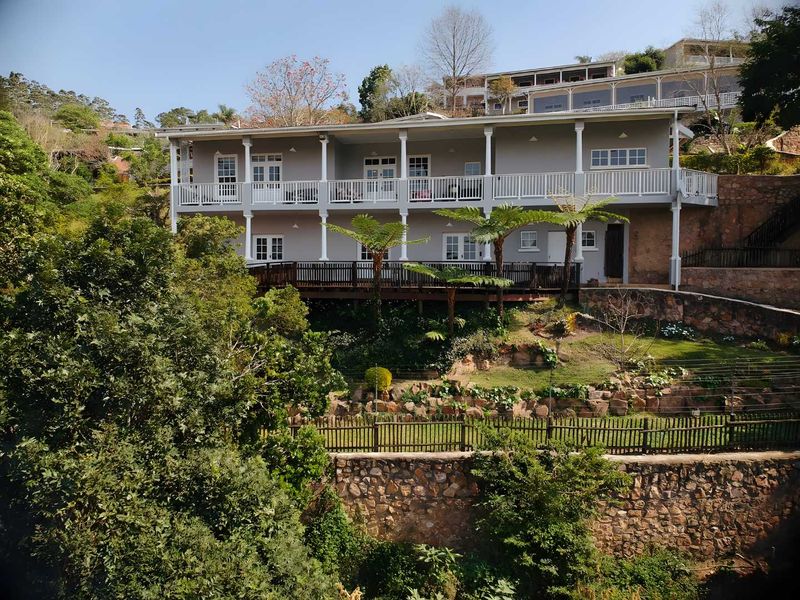 Rear view of a double-story townhouse featuring extensive timber decking, balconies, and tiered stone retaining walls set within a landscaped garden.