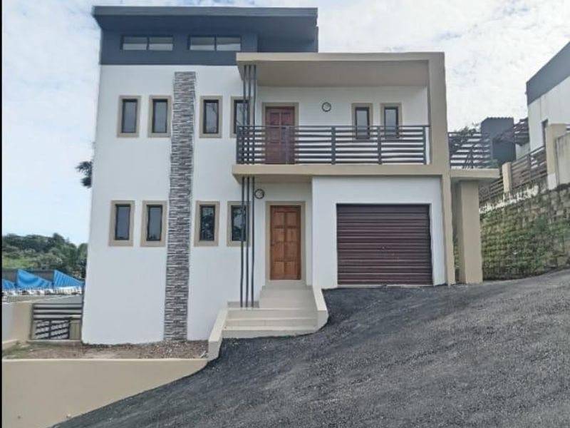 Modern double-story townhouse facade featuring a garage, upper-level balcony with metal railing, and decorative stone cladding accents.