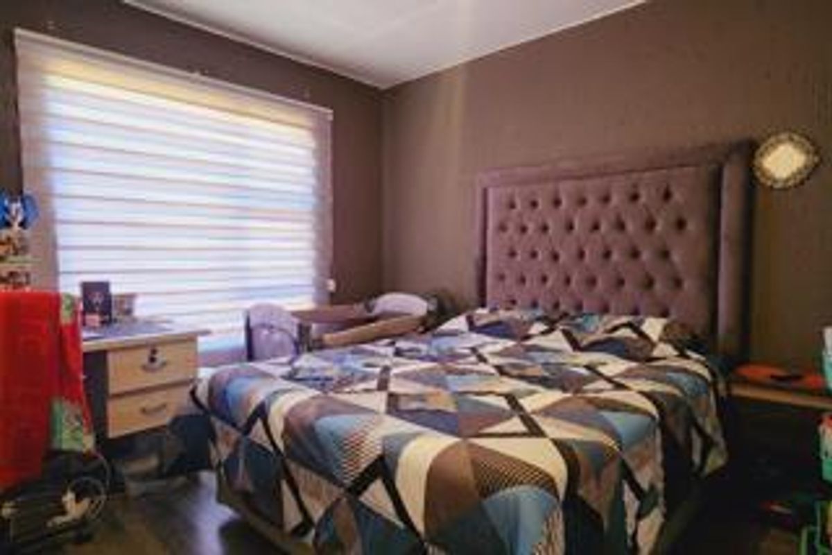 A bedroom featuring dark-toned walls, a large window with fitted blinds, and laminate flooring.