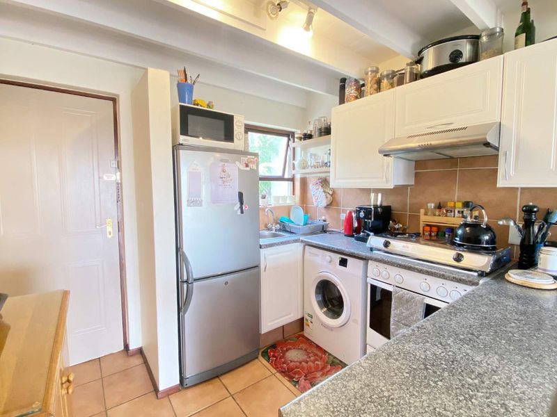 Compact kitchen featuring built-in cabinetry, tiled backsplash, integrated stove and oven, and tiled flooring with exposed ceiling beams.