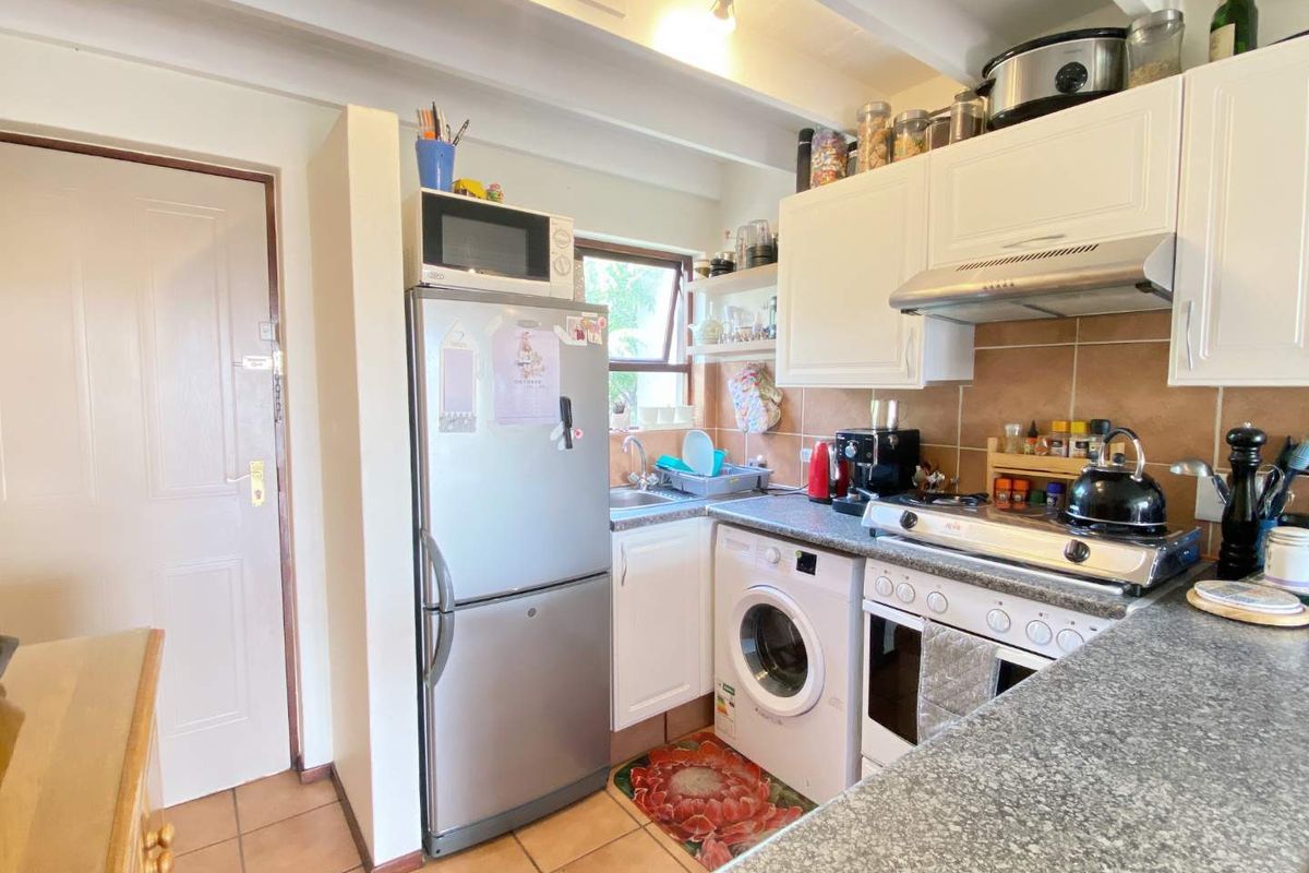 Compact kitchen featuring built-in cabinetry, tiled backsplash, integrated stove and oven, and tiled flooring with exposed ceiling beams.