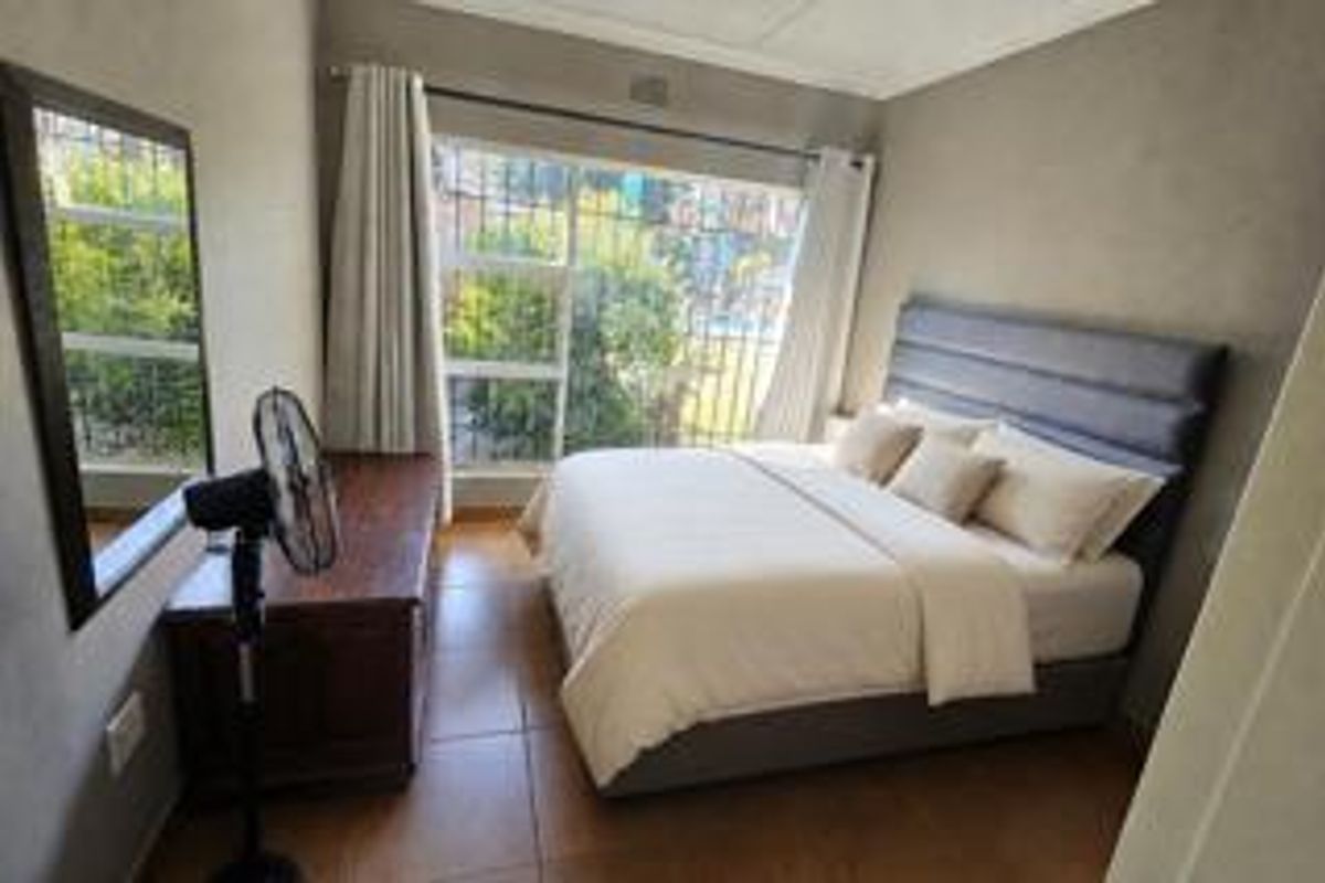 A well-lit bedroom featuring tiled flooring and a large window with security bars, providing a comfortable and functional living space.