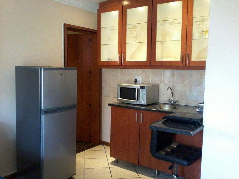 Compact kitchen area featuring wooden cabinetry, tiled backsplash, integrated sink, and tiled flooring.