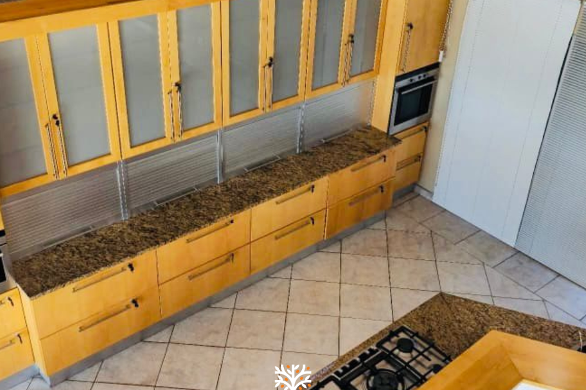A high-angle view of a kitchen featuring light wood cabinetry, granite countertops, a built-in oven, and a gas hob set into a central island.