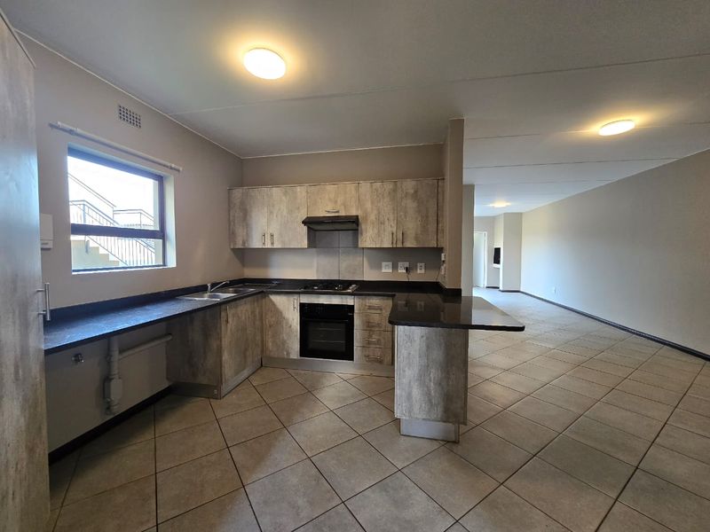 Spacious open-plan kitchen featuring modern wood-look cabinetry, dark laminate countertops, built-in oven, and hob, flowing seamlessly into an expansive living area with tiled floors.