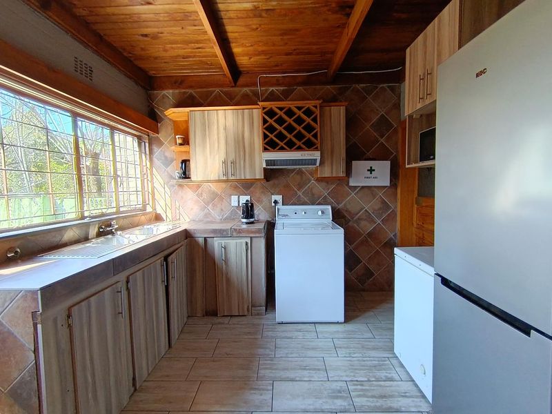 A functional kitchen featuring timber ceilings, tiled splashbacks, built-in cabinetry with integrated wine rack, and tiled flooring with large windows.