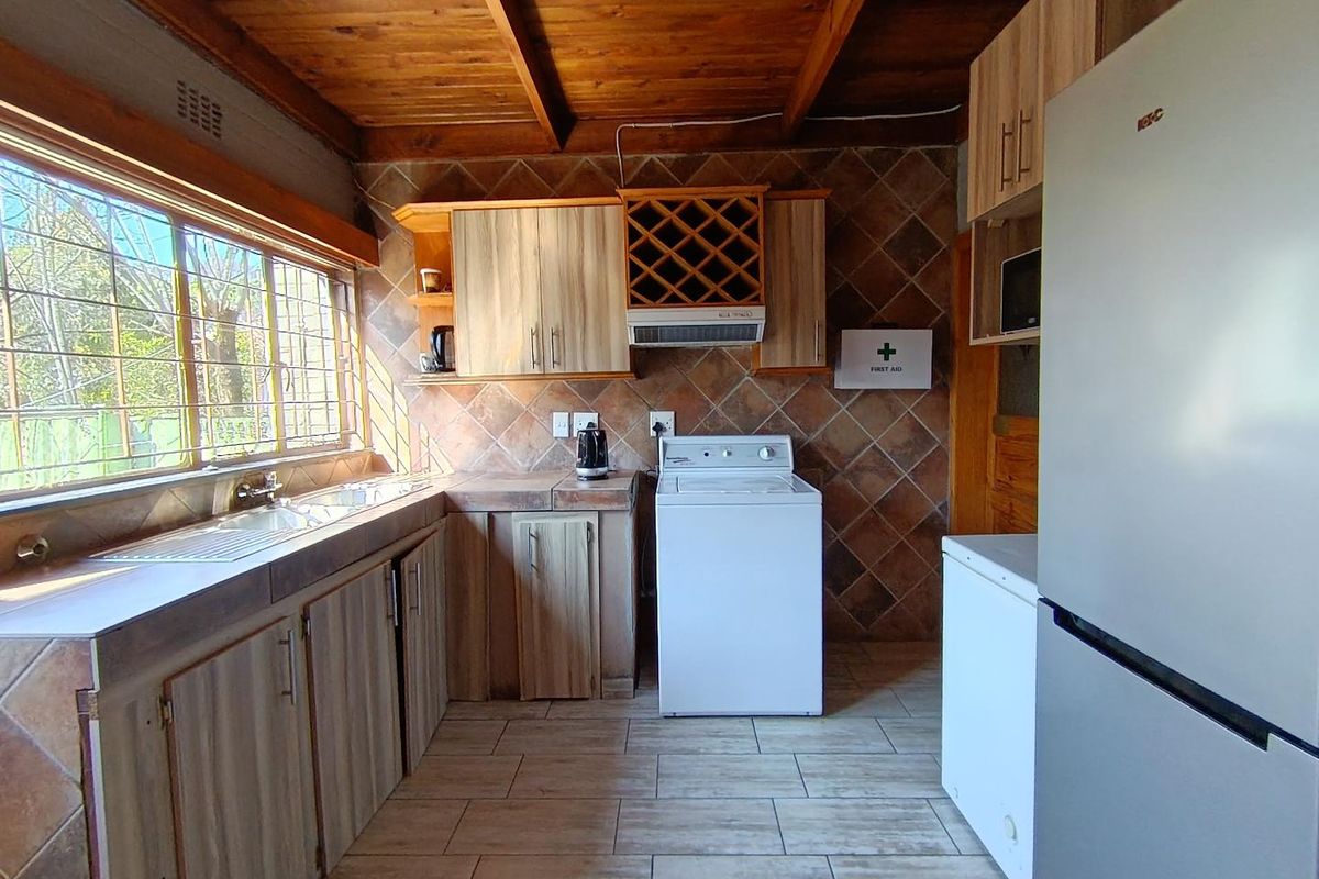 A functional kitchen featuring timber ceilings, tiled splashbacks, built-in cabinetry with integrated wine rack, and tiled flooring with large windows.