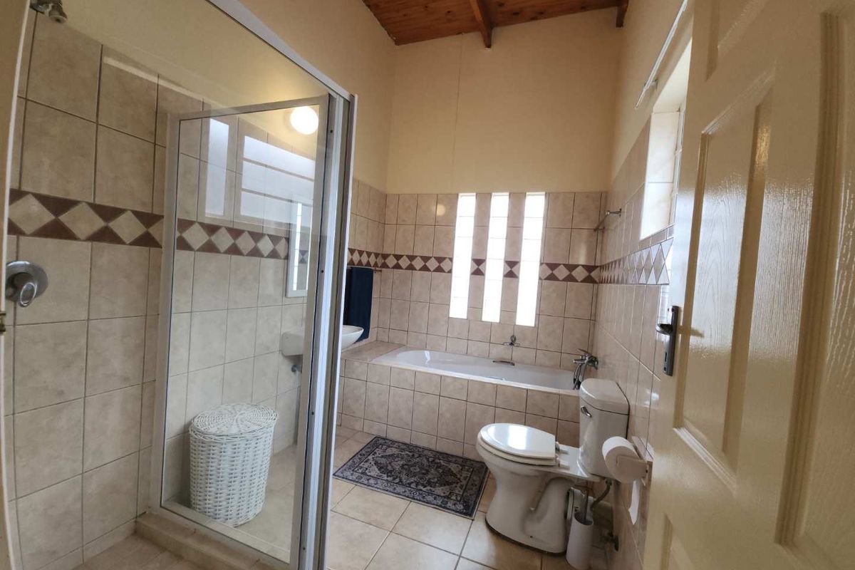 A functional bathroom featuring a built-in bathtub, separate glass-enclosed shower, toilet, and basin, finished with neutral wall tiles and a timber-paneled ceiling.