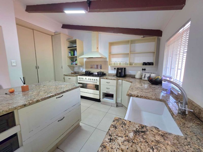 A functional kitchen featuring granite countertops, a farmhouse sink, gas stove with extractor, and exposed timber ceiling beams, offering a classic aesthetic.