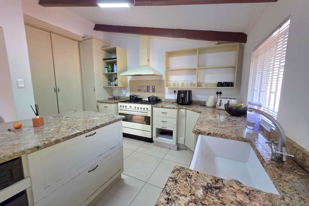 A functional kitchen featuring granite countertops, a farmhouse sink, gas stove with extractor, and exposed timber ceiling beams, offering a classic aesthetic.