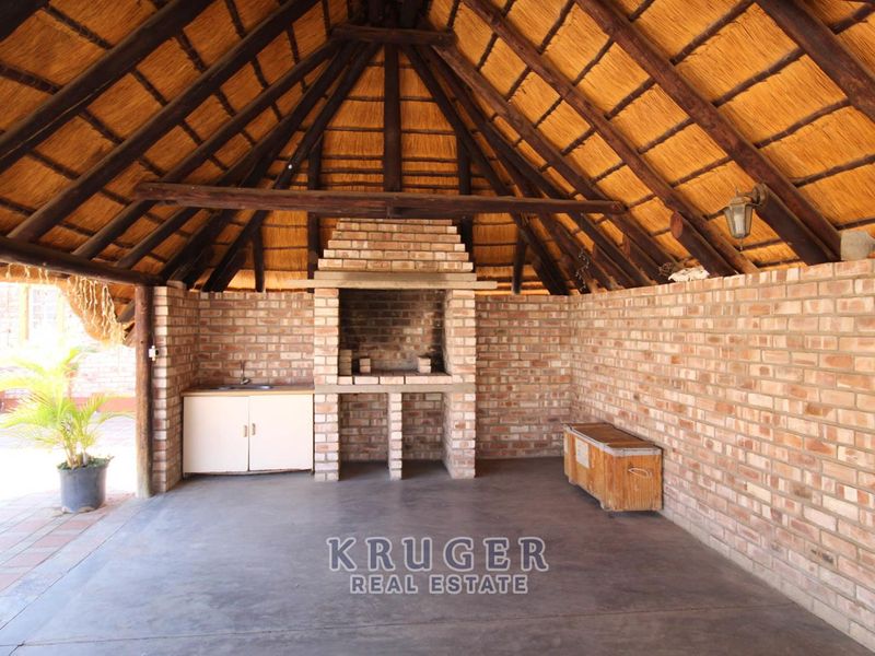 Covered outdoor entertainment area featuring a traditional thatched roof, exposed timber beams, and a built-in brick braai with a prep area and sink.