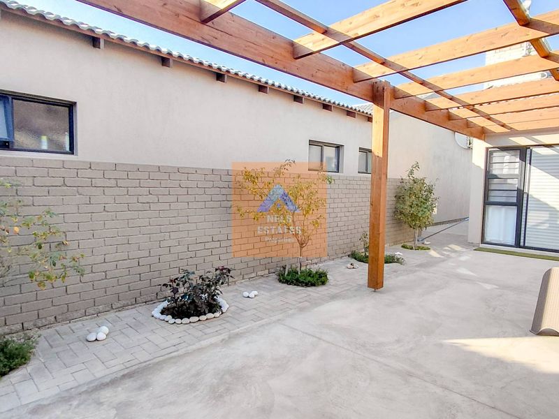 A well-maintained outdoor patio area featuring a timber pergola, paved flooring, and direct access to the interior through sliding glass doors.