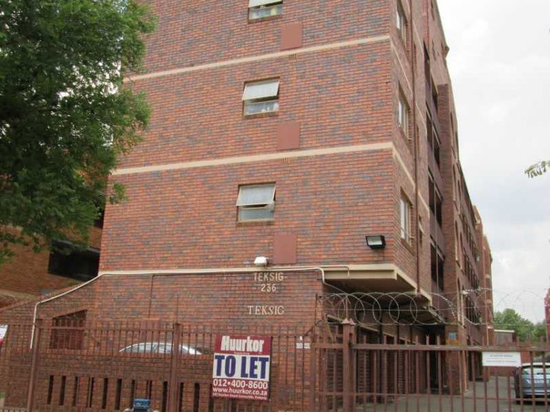 Exterior view of a multi-story face brick apartment building featuring secure gated access and perimeter fencing.