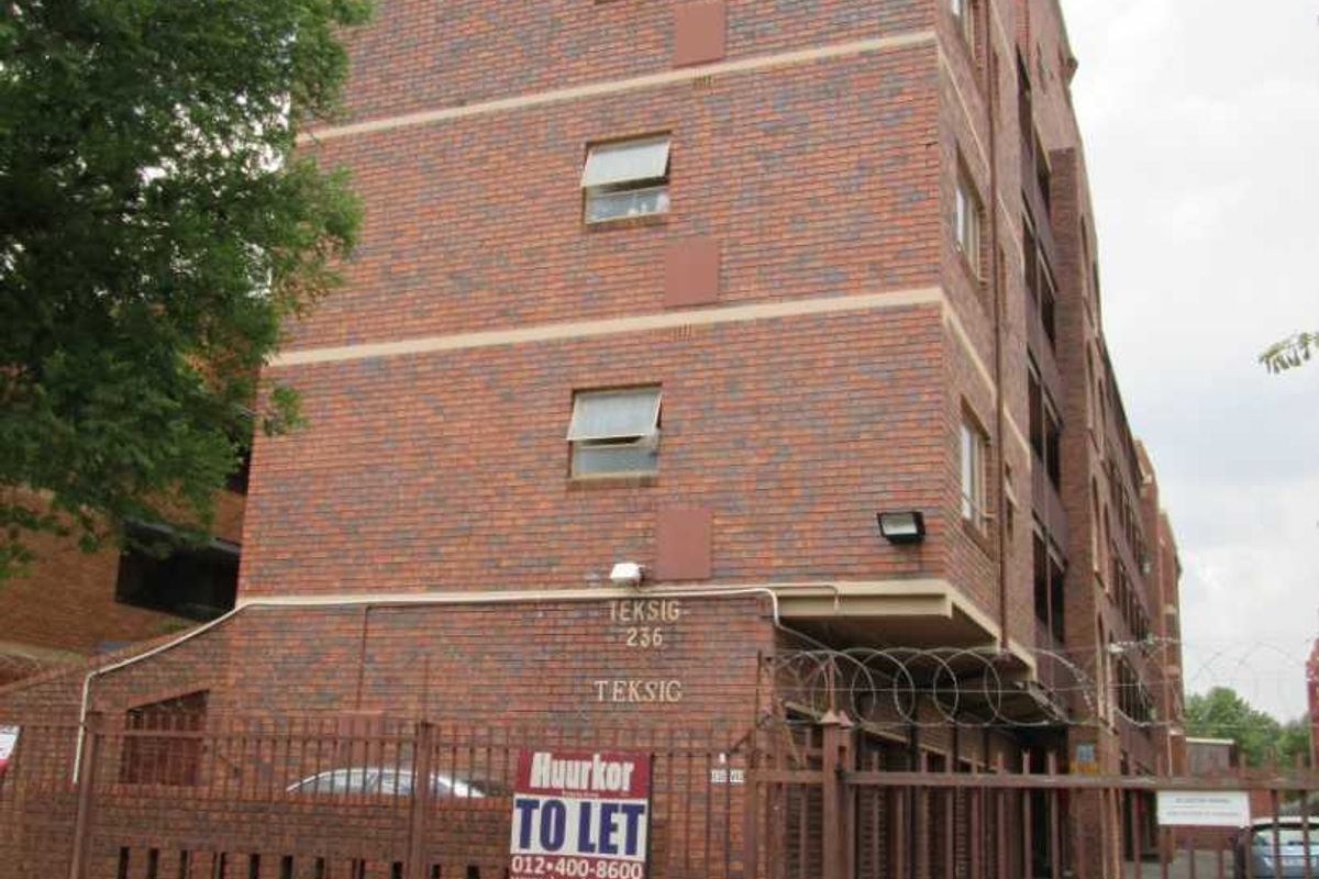 Exterior view of a multi-story face brick apartment building featuring secure gated access and perimeter fencing.