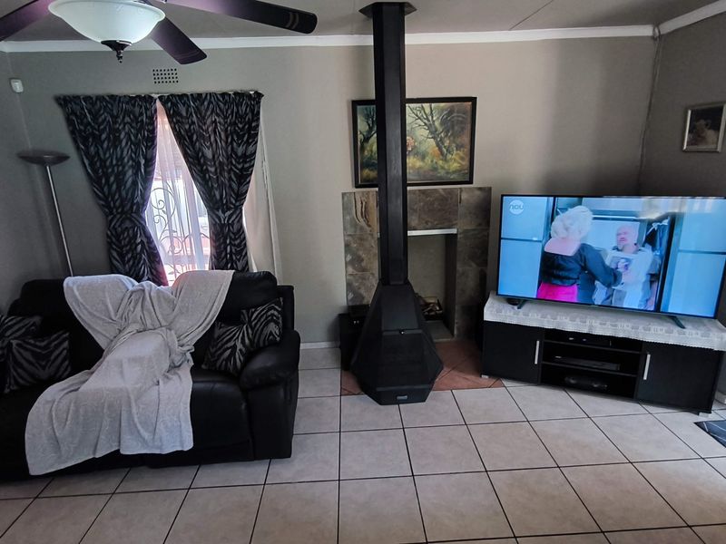 A living room featuring a central freestanding fireplace with a stone surround, tiled flooring, and a ceiling fan.