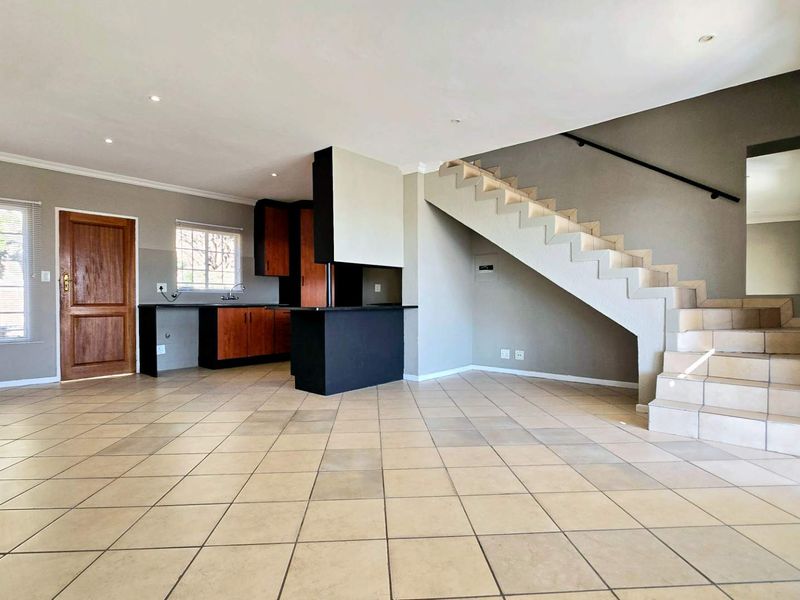 Spacious open-plan living area featuring tiled flooring, a functional kitchen with built-in cabinetry, and a staircase leading to the upper level.