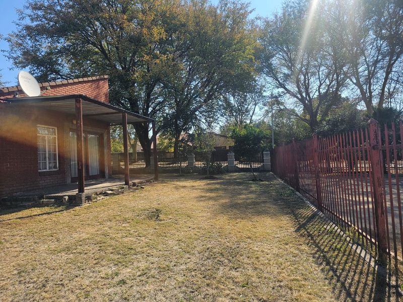 Rear view of a brick house featuring a covered patio area, a large garden space, and perimeter steel fencing.