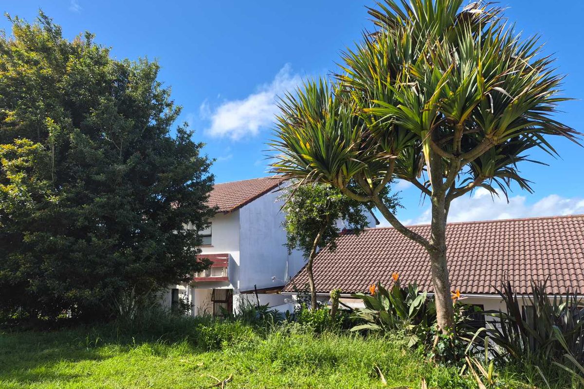 A view of the rear exterior of the house featuring a tiled roof, plastered walls, and established garden greenery.